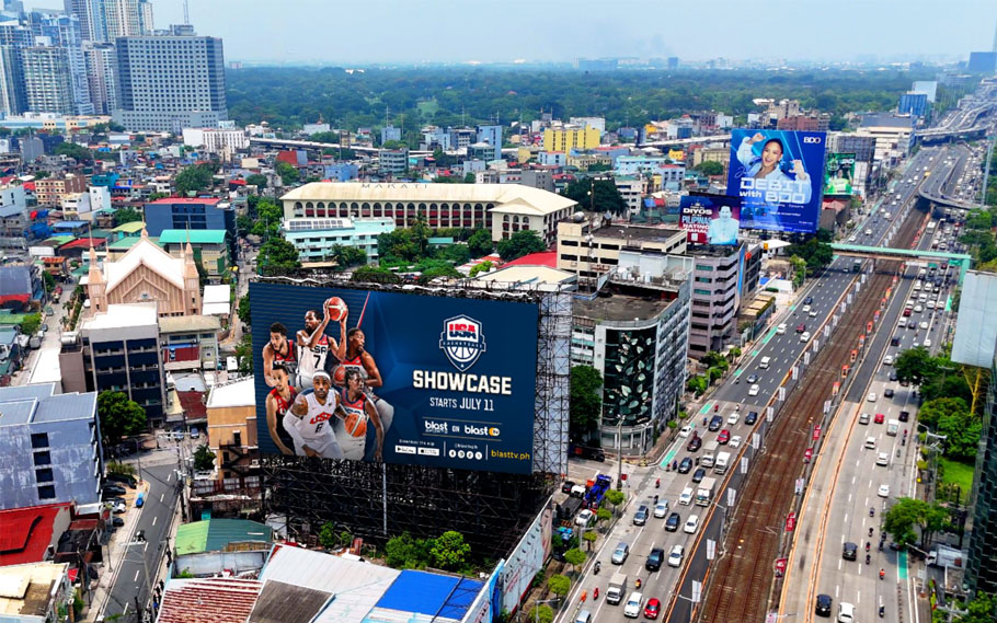 Massive roadside LED billboard in Manila promoting USA Basketball Showcase, featuring NBA players and set against a busy urban skyline with high-rise buildings and a major highway.