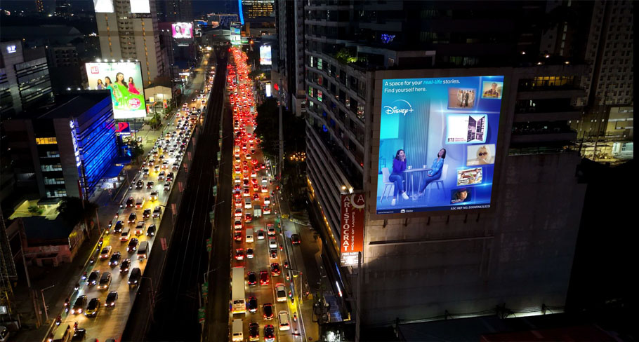 Illuminated Disney+ digital billboard on a high-rise building in Metro Manila at night, overlooking heavy traffic and vibrant city lights along EDSA