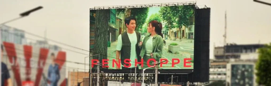 a man and a woman, standing outside on a tree-lined European-style street, promoting the Penshoppe brand.